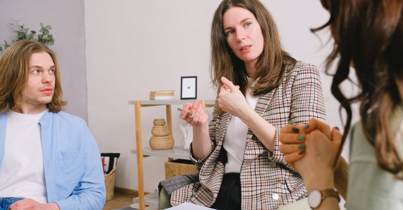Client Relationships - Thoughtful woman psychologist in stylish clothes siting with clipboard and talking with couple in light room