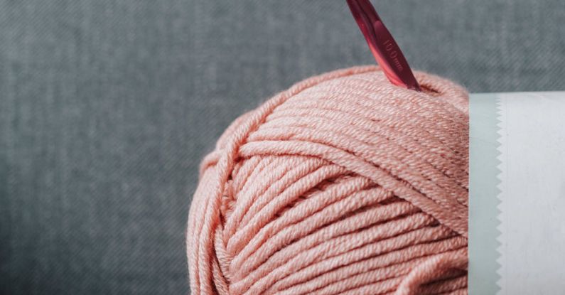 Soft Skills - Ball of soft yarn for knitting with pink crochet hook on gray comfortable couch at home