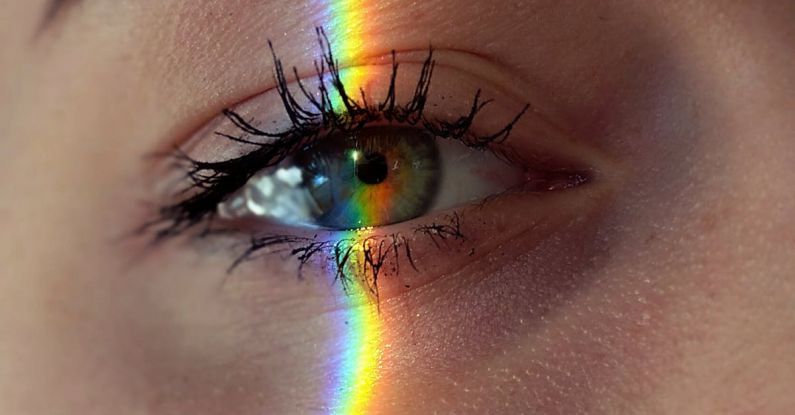 Problem-Solving - Closeup of crop anonymous sad female with green eyes and rainbow light on face looking at camera
